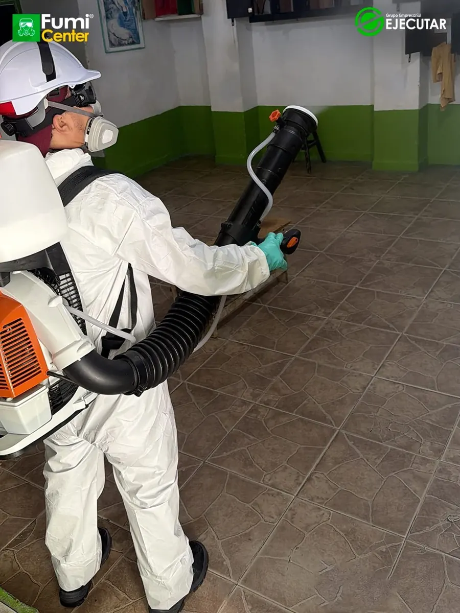 Técnico de FumiCenter con traje de protección y pulverizador aplicando en instalaciones del INPEC